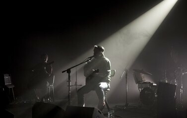 Paweł Domagała w ciemnym świetle grający na gitarze i śpiewający do mikrofonu